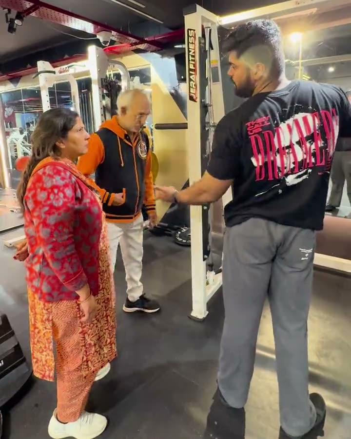 Coach Sar, in a black T-shirt, coaching a senior couple through squats and lat pulldowns